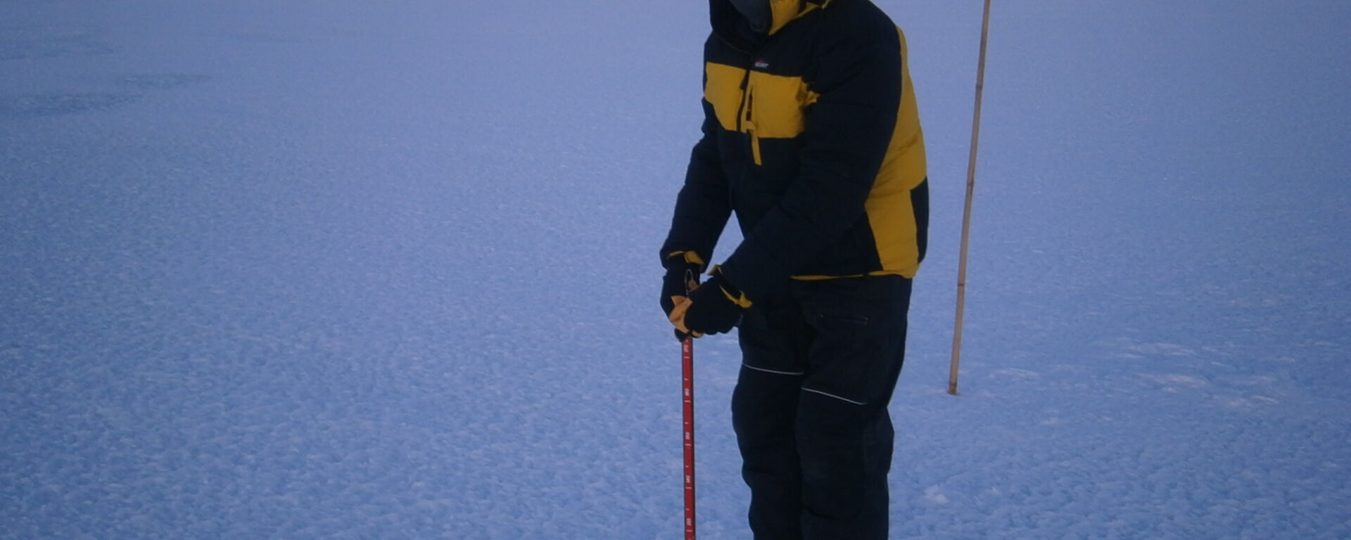 An expeditioner has lowered his gauge down the drilled hole and is about to read the ice thickness on the scale
