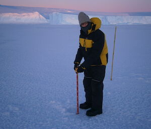 An expeditioner has lowered his gauge down the drilled hole and is about to read the ice thickness on the scale