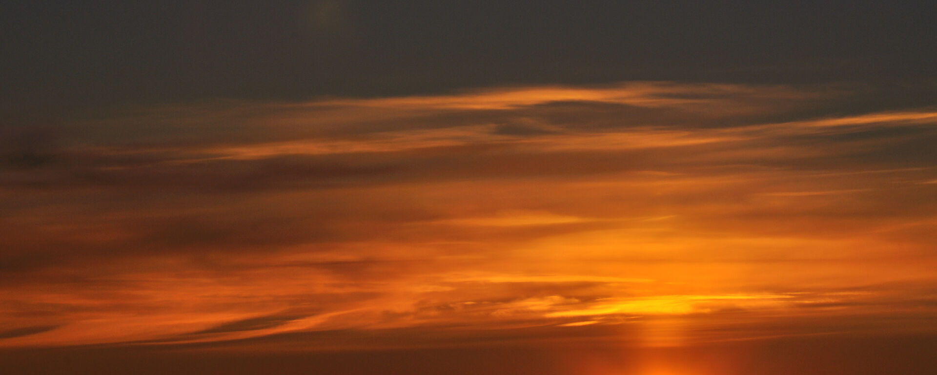 A brilliant orange yellow sky with the sun on the horizon and images of icebergs beneath it
