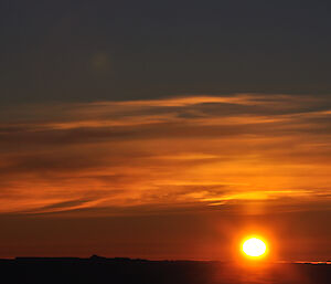 A brilliant orange yellow sky with the sun on the horizon and images of icebergs beneath it