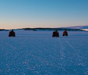 Three expeditioners riding quad bikes on the sea-ice with an island behind them and the icy plateau on the right in the background