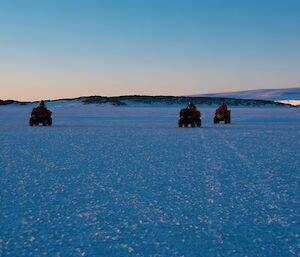 Three expeditioners riding quad bikes on the sea-ice with an island behind them and the icy plateau on the right in the background