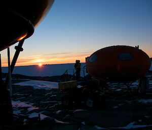The setting sun with dark images of an expeditioner, the 2 smarties and a quad in the foreground