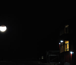 The moon with the top third in shadow is in teh sky on the left with an image of the Red Shed building and its lights on the right