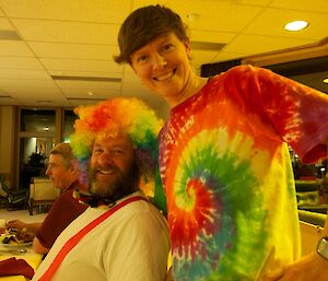 A female expeditioner wearing a multi-coloured top next to a male expeditioner with a similarly coloured wig, bow tie and apron