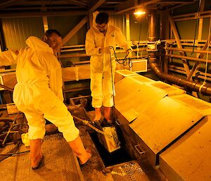 Two expeditioners lifting a dredge full of sludge from a sewage tank