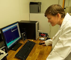 A female expeditioner in white lab coat reading the plot from the detector on a computer screen