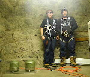 Two green dome shaped seismic monitors in a plastic cabinet inside a vault with 2 expeditioners in full body harnesses standing alongside the monitors