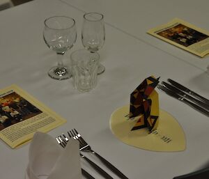 An individual place setting with menu, information booklet and origami penguin