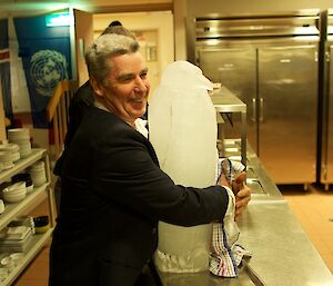 An expeditioner ablout to carry a large ice sculpture of an emperor penguin to form a centre piece for the table