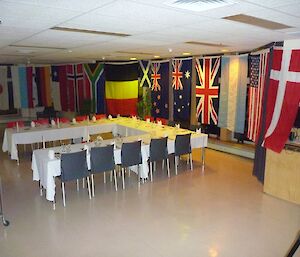 The table placed in U shape with tablecloths and place settings and the walls of the dining room decorated with the Antarctic Treaty Nations’ flags