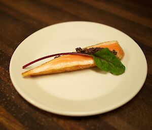 A piece of salmon with an olive tapenade and a beet leaf for decoration