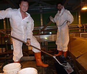 Two expeditioners in protective suits removing sludge with a special dredge in the Waste Treatment Plant