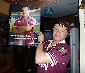 An expeditioner holding a Queensland WorkCover poster signed safety ambassador Mal meninga