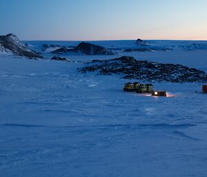 Hut and vehicles on snowy island with rocky outcrops in background
