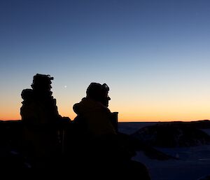 Two silhouettes with an orange sky behind them