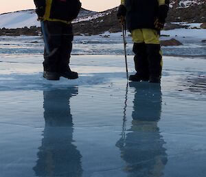Two people standing with reflections in frozen lake ice