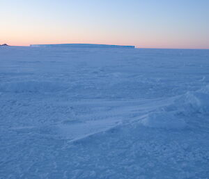 Sea ice covered in snow with pink sky