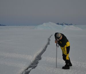 Person with drill on sea ice next to tide crack