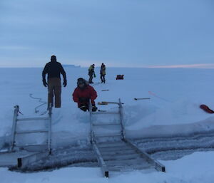 Several people on sea ice setting ramps across a crack in the ice