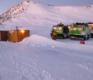 Two vehicles on snow outside a hut