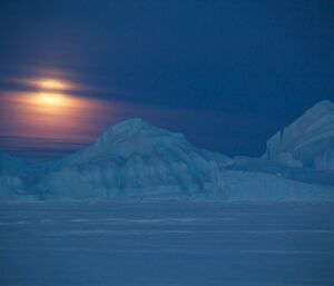 Moon setting behind an ice berg