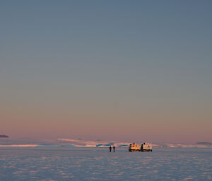 The Hägglunds and people are on the sea ice with the Antarctic plateau to the left (south) with the summits of the Framnes Mountains rising above the plateau