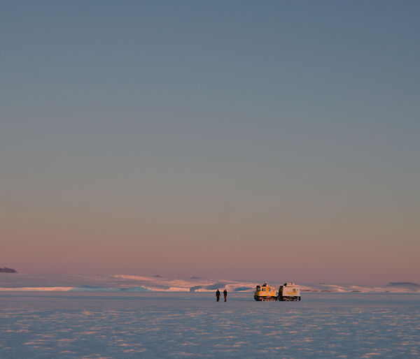 The Hägglunds and people are on the sea ice with the Antarctic plateau to the left (south) with the summits of the Framnes Mountains rising above the plateau