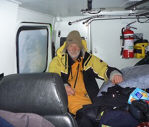 An expeditioner in full Antarctic winter clothing sitting in a heated Hägglunds whilst outside the emperor penguins battle the elements