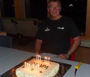 A male expeditioner sitting at the dinner table with his birthday cake and candles in front of him on the table
