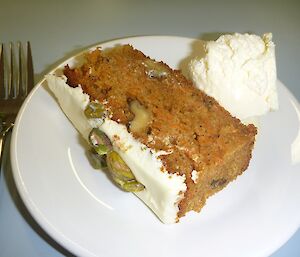 A slice of Wayne’s carrot and walnut cake decorated with icing and pistachio nuts and accompanied with ice cream