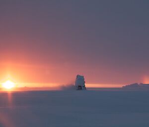 An oversnow vehicle driving away in the distance with the sun on one side and coloured rainbow band on the other