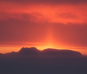 Bright orange and pink sky with pillar of light rising upwards from a bright solar disc