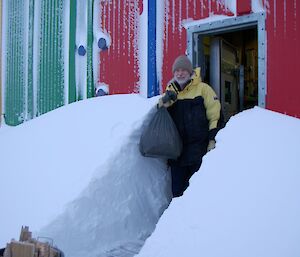 An expeditioners carrying a bag of rubbish from the multi coloured carpenter’s workshop after a heavy fall of snow