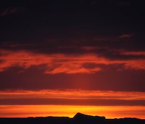 The sun just dipping below the horizon with icebergs in the foreground and the sky a brilliant red and orange