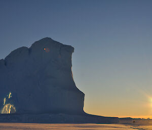 An iceberg with an interesting feature in it and with 3 expeditioners walking on the sea-ice