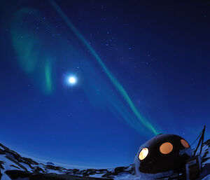The Macey red Apple Shelter at night with the moon and green curtains of an aurora