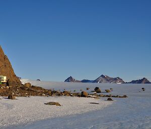 A small green Rundoodle field hut nestled against the Northern Masson Range with the peaks of the David Range to the west with the ice sheet in the foreground