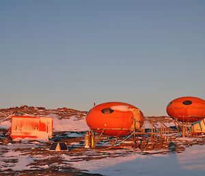 A small wooden toilet, an orange container on a sledge, the 2 Smarties (Googies) and a white Apple Shelter on Bechervaise Island