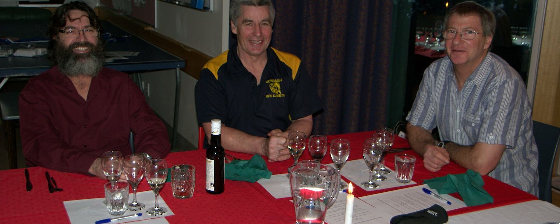 Three people sitting talking at a dinner table with wine tasting glasses in front of them