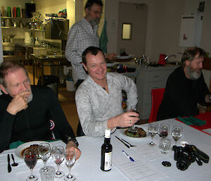 Three expeditioners discussing the finer points of wine tasting whilst another expeditioner behind them serves meals