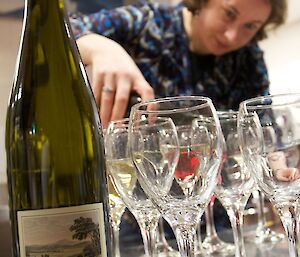 A person pouring wine into a collection of glasses with the wine bottle in the foreground