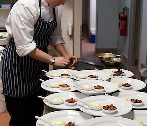 Chef standing next to a collection of plates on which she is preparing food