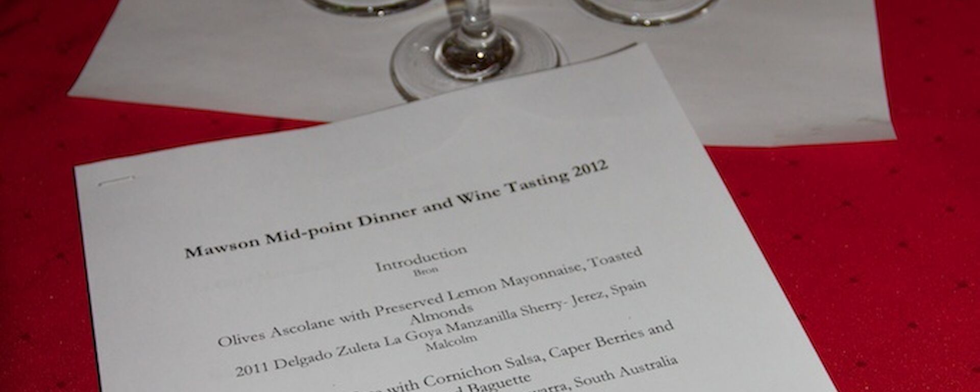Five glasses of wine arranged for tasting with a menu lying in front of them on a dinner table