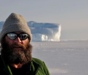 A photo of an expeditioner at Auster with a reflection of the photographer and icebergs in the right side of his sunglasses and a reflection of people and Hägglunds in the left side