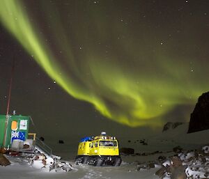 Hut and Hägglunds with green aurora lights in the sky above them