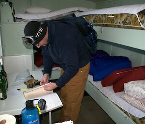 Person signing a book on a table in a small hut