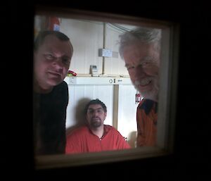 Three people seen through a small window in a door