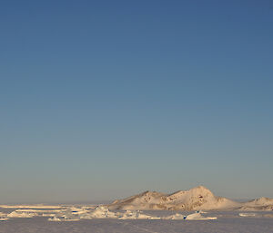 A large bluff-shaped island with a glacier to the left and sea-ice in the forground