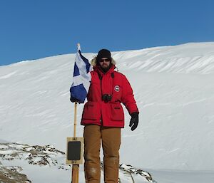 An expeditioner born in Scotland standing beside the Scottish flag at Cape Bruce